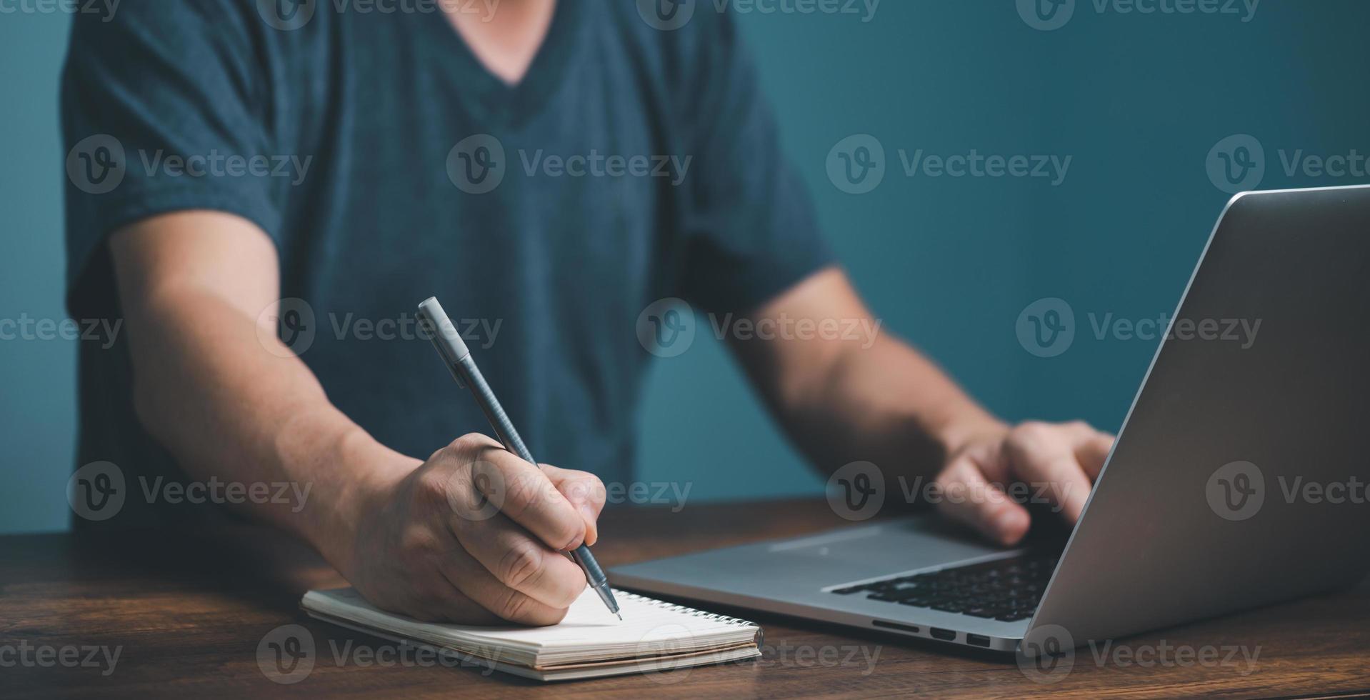 E learning concept. Casual business man studying online course via laptop computer and writing on notebook. photo