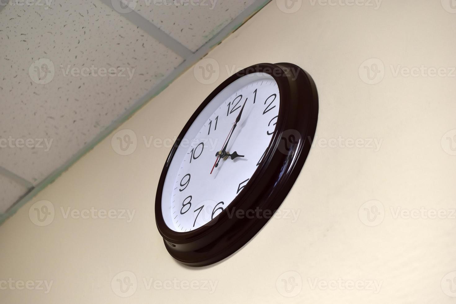 A black round clock with a white dial on a light wall. photo