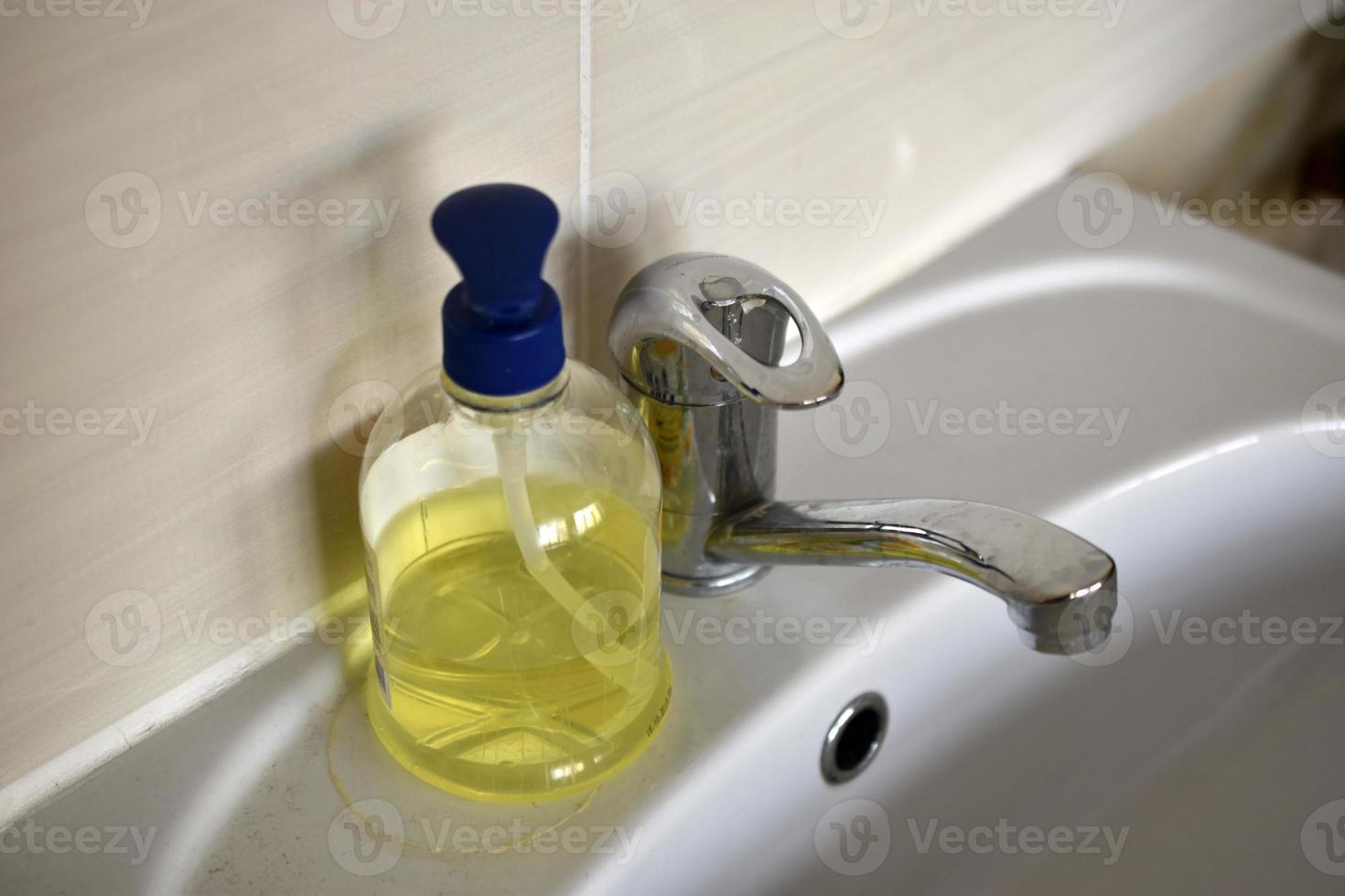 A shiny faucet with water and a washbasin with liquid soap in the room. A place for washing and soap. photo