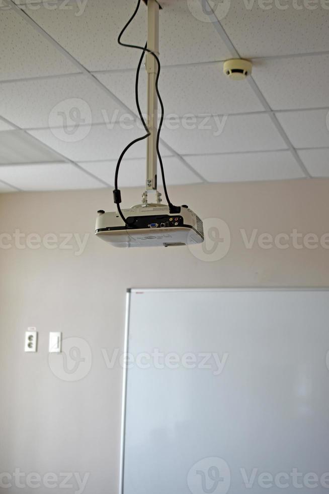 A white projector in a small hall in the school opposite the blackboard. An office with a projector. A projector hangs from the ceiling. photo