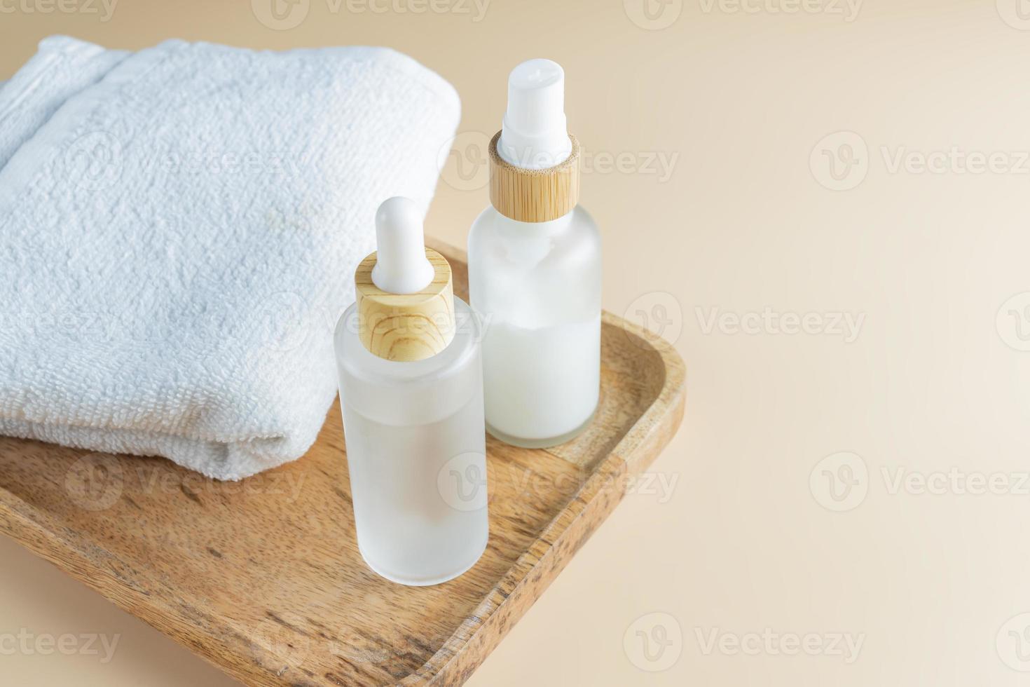 Skin care set in frosted glass bottles on wooden tray with towels. Beauty treatment routine mockup. Spa concept photo