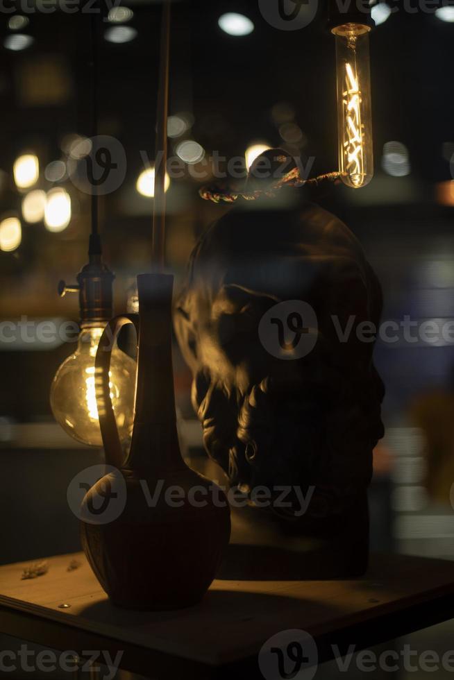 Sculpture of head with lamps. Jug on table. Incandescent lamps in interior. photo