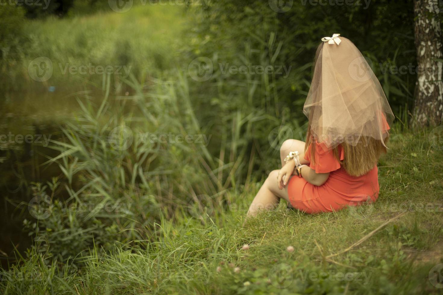 Girl on shore of lake in summer. Maiden in orange clothes. Bride in dress. Holiday in park. photo