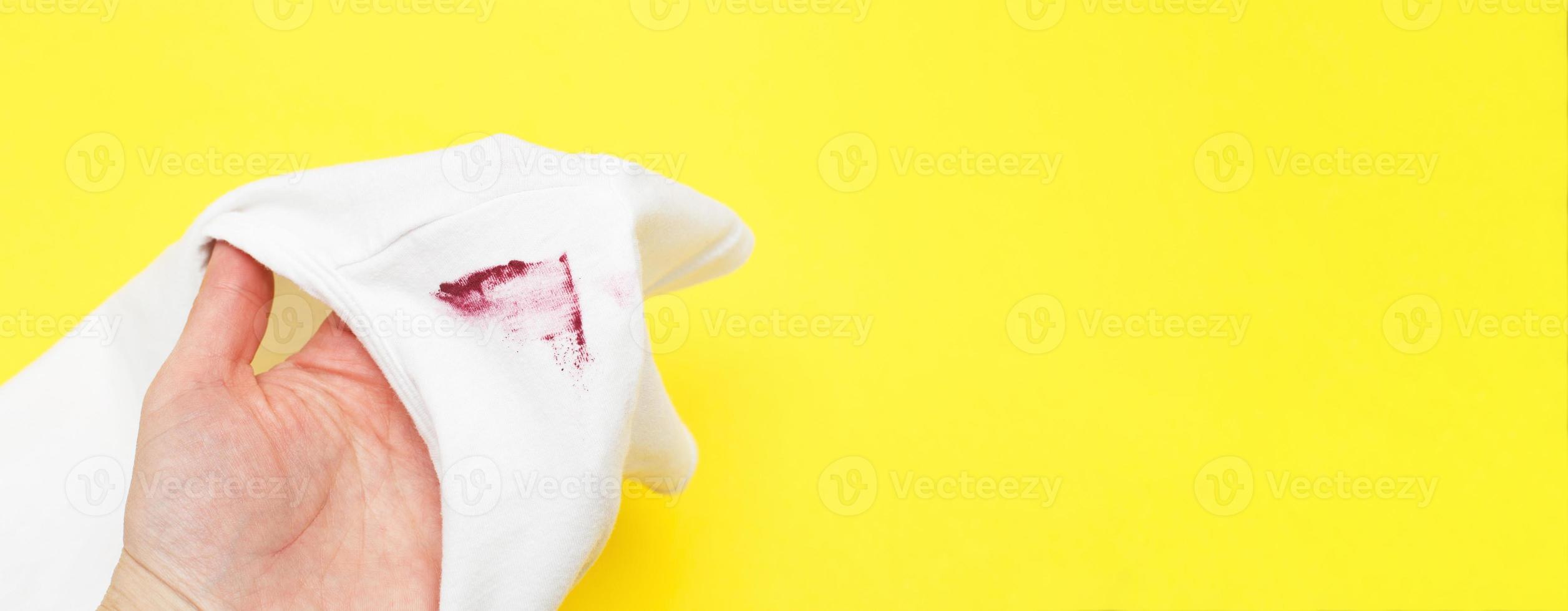 female hand holding white shirt with red lipstick stain on yellow background photo