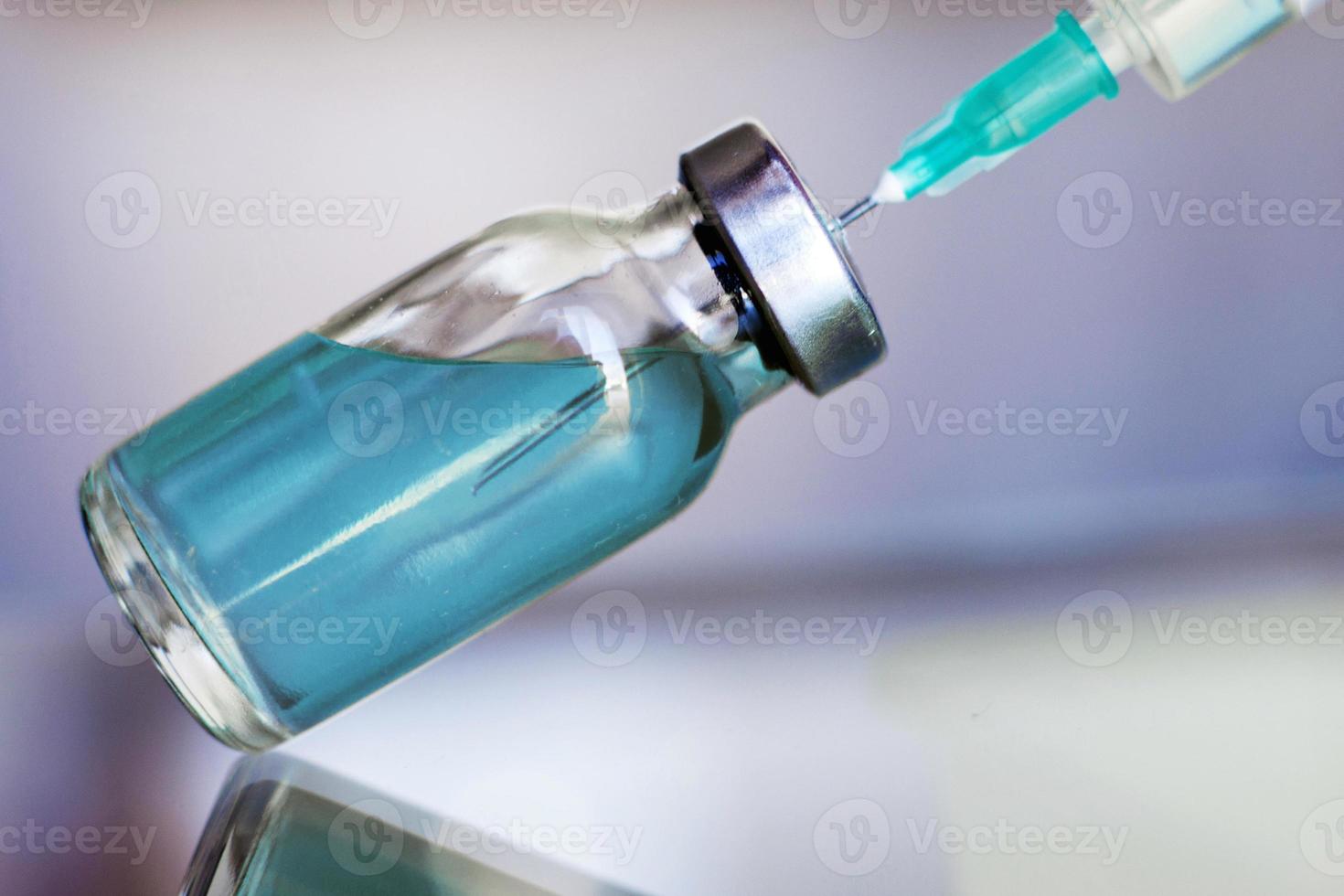 Vial filled with liquid vaccine in medical lab with syringe. medical ampoule and syringe on the glass surface photo