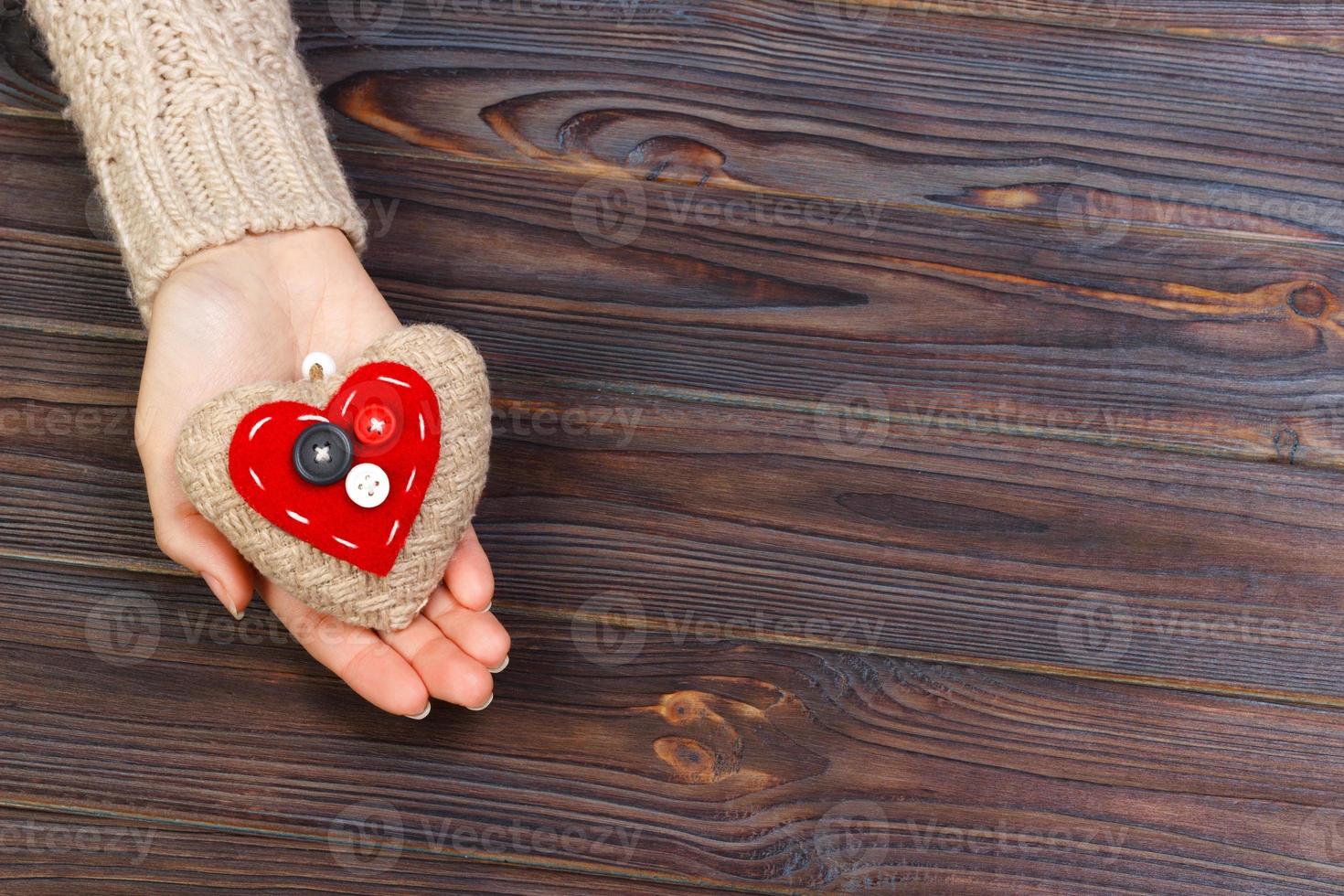 Woman's hands with beautiful accurate knitted red heart. White cozy knitted sweater on wooden background. Concept of giving help. Love concept with copyspace photo