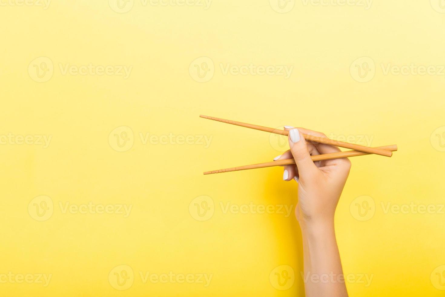 palillos de madera sostenidos con manos femeninas sobre fondo amarillo. listo para comer conceptos con espacio vacío foto