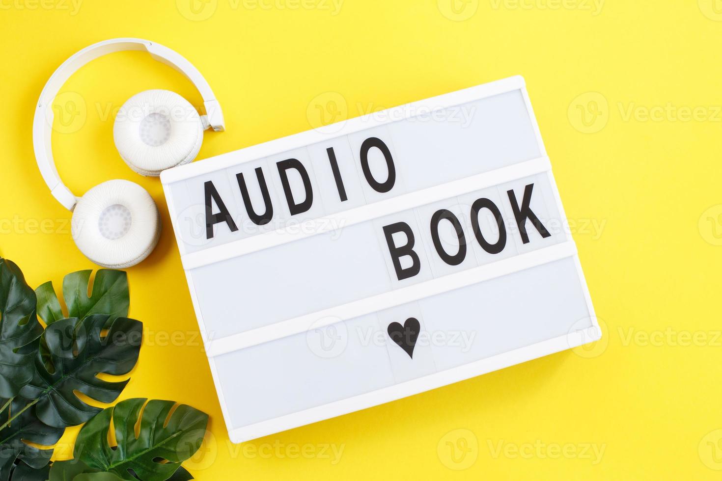 inscription audiobook on a light box with modern white headphones on a yellow background photo