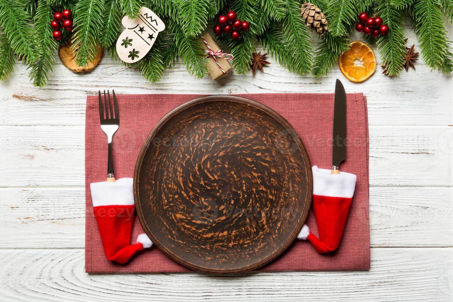 Top view of Christmas dinner on wooden background. Plate, utensil, fir tree and holiday decorations with copy space. New Year time concept photo