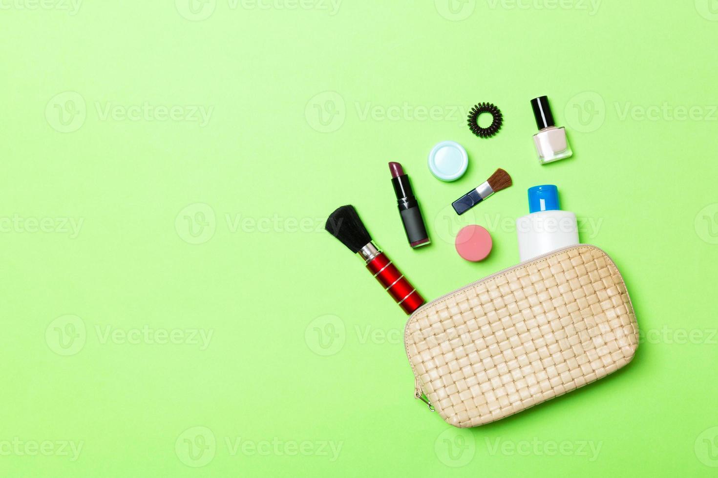 Aerial view of a leather cosmetics bag with make up beauty products spilling out on green background. Beautiful skin concept with copy space photo