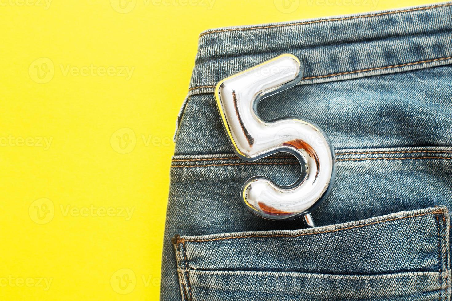 number 5 sticking out of the back pocket of blue jeans on yellow background photo