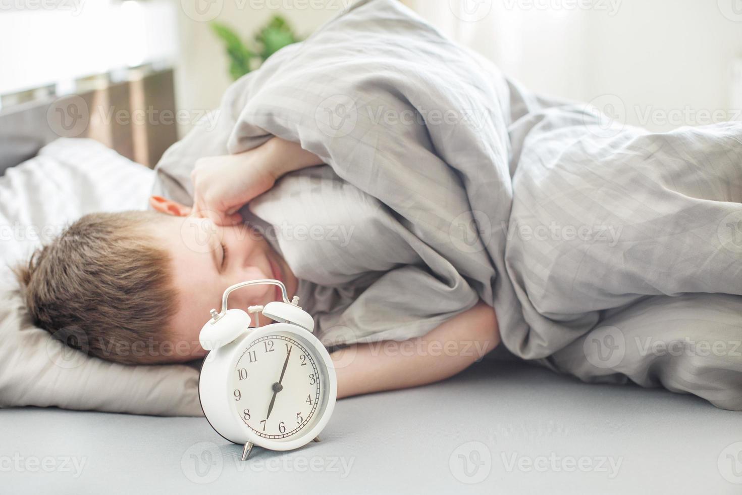 the boy lies on the bed in morning and covers his ears so as not to hear the alarm clock. child does not want to wake up photo