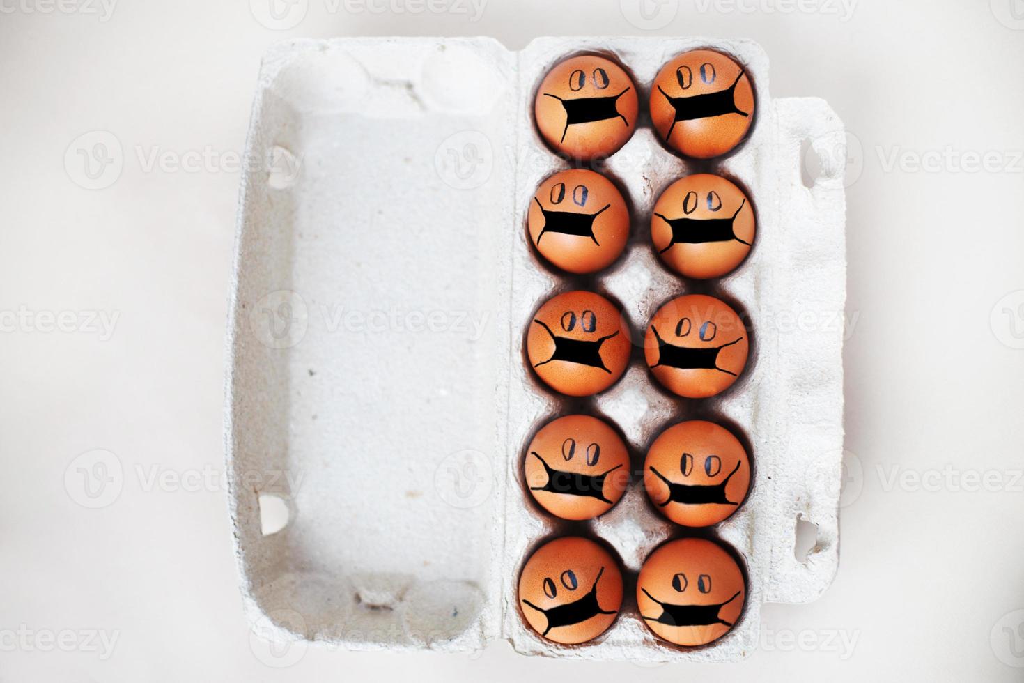 chicken eggs with drawn medical mask on egg carton on white background. Easter eggs holidays decoration. photo