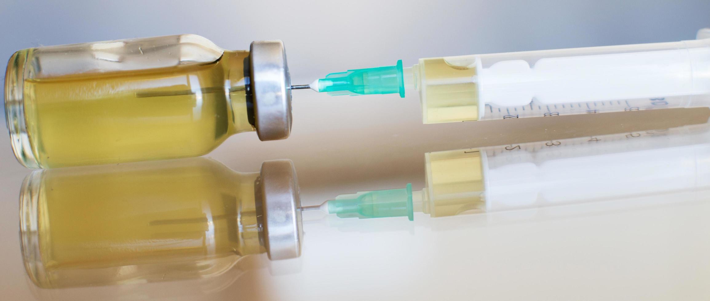 vial lleno de vacuna líquida en laboratorio médico con jeringa. ampolla médica y jeringa en la superficie de vidrio. bandera foto