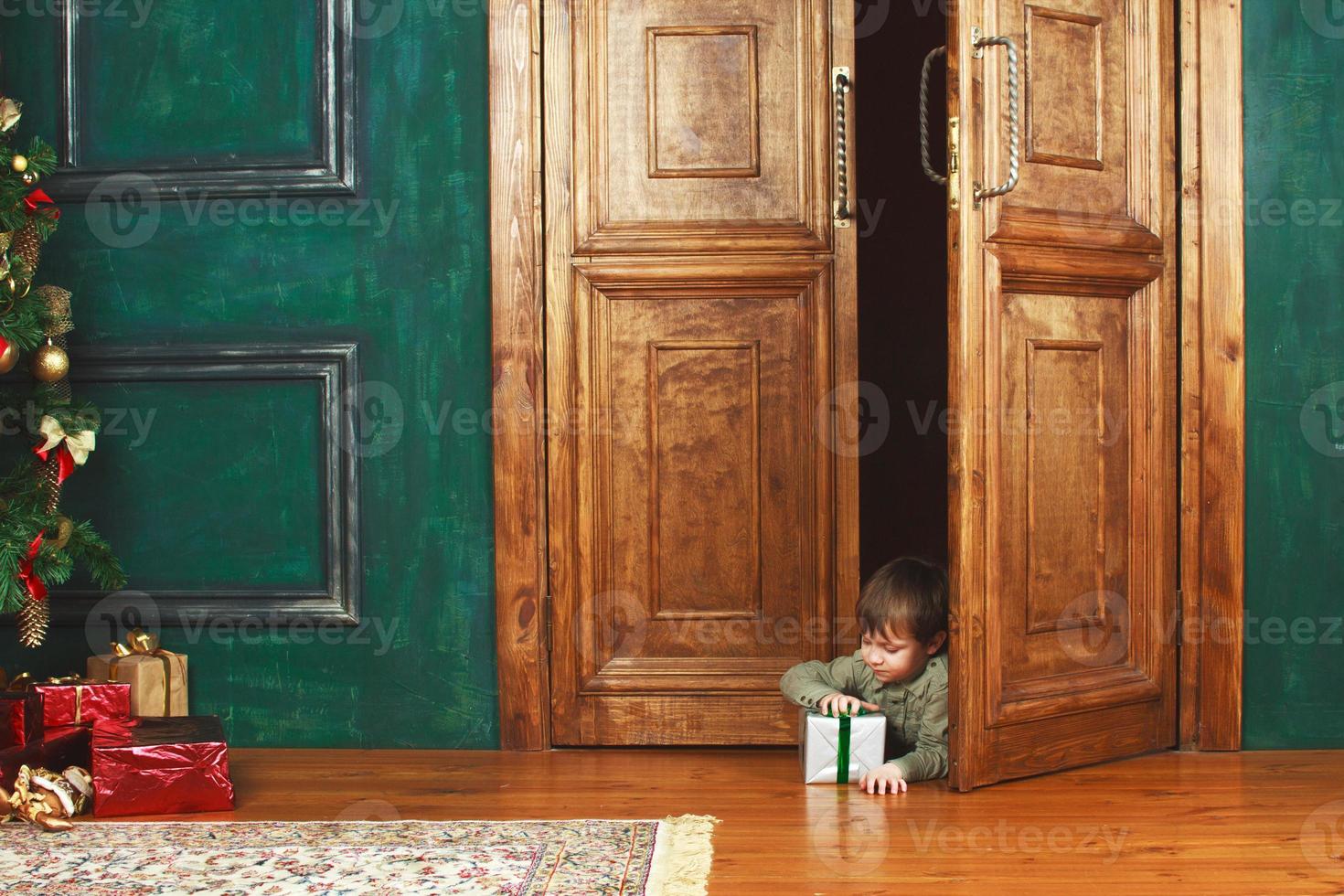 niño se asoma por la puerta con una caja de regalo de navidad. foto