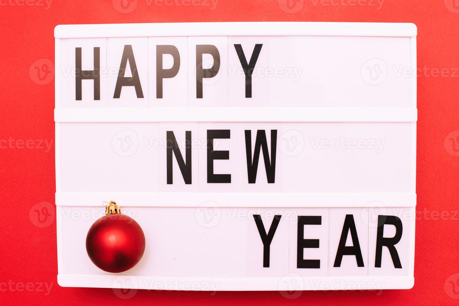 The inscription happy new year on a light box with Christmas toy ball on a red background. photo