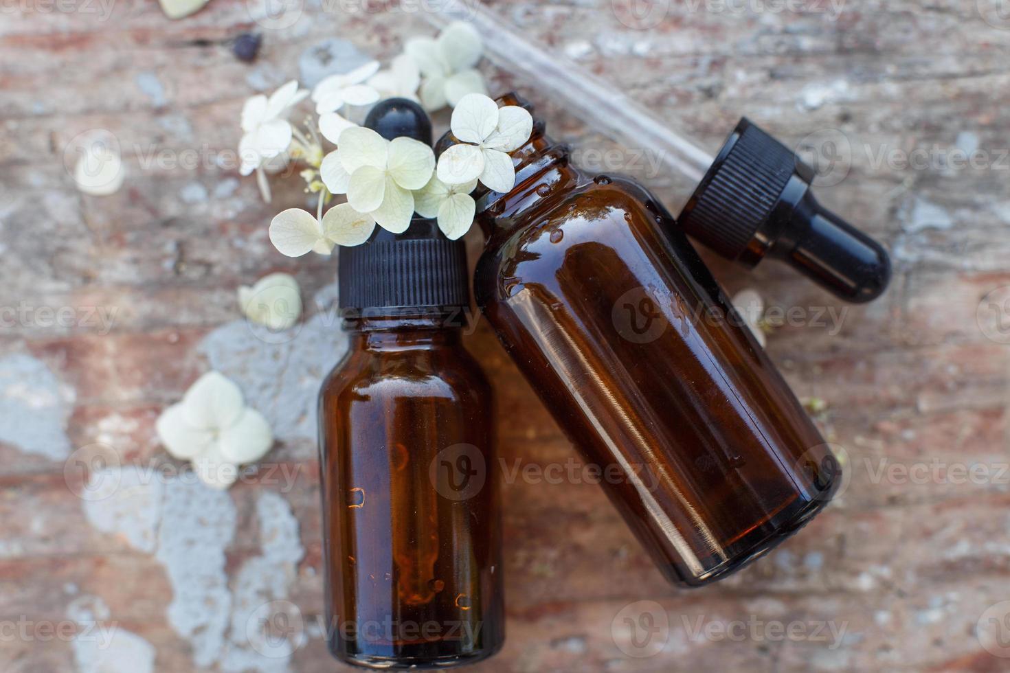 botellas de vidrio marrón de aceite esencial y hortensias de flores blancas sobre fondo de madera antiguo foto