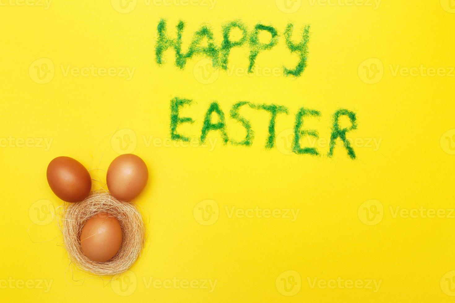 inscription happy easter from grass with bunny eggs and nest on yellow background photo