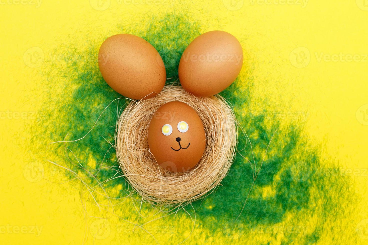 happy easter bunny eggs in nest on the decorative grass on yellow background. copy space for text photo