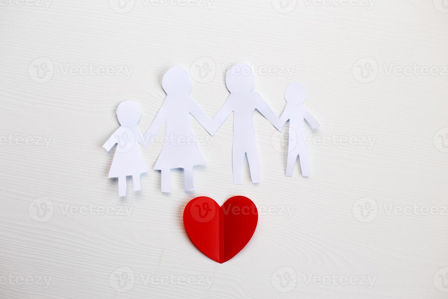 Happy paper cut family holding hands on a light wooden background with red heart. photo