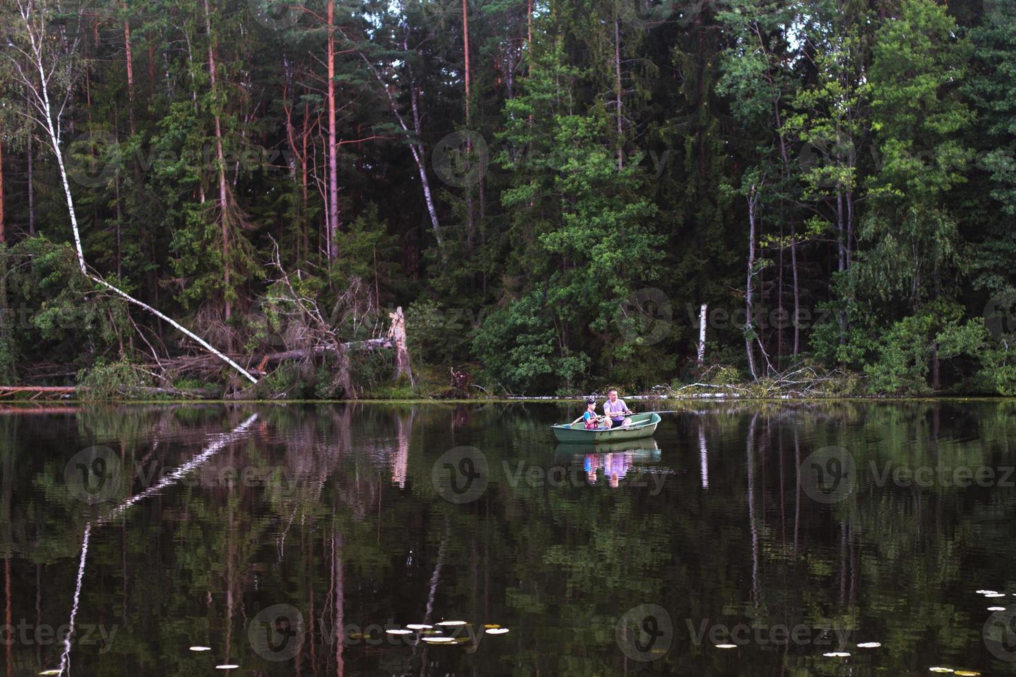 Father and son fishing on rural lake at sunset on a boat photo