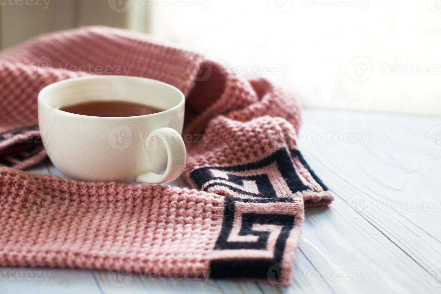 taza de café caliente con suéter de punto en una mesa de madera cerca de la ventana, concepto de mañana de invierno foto
