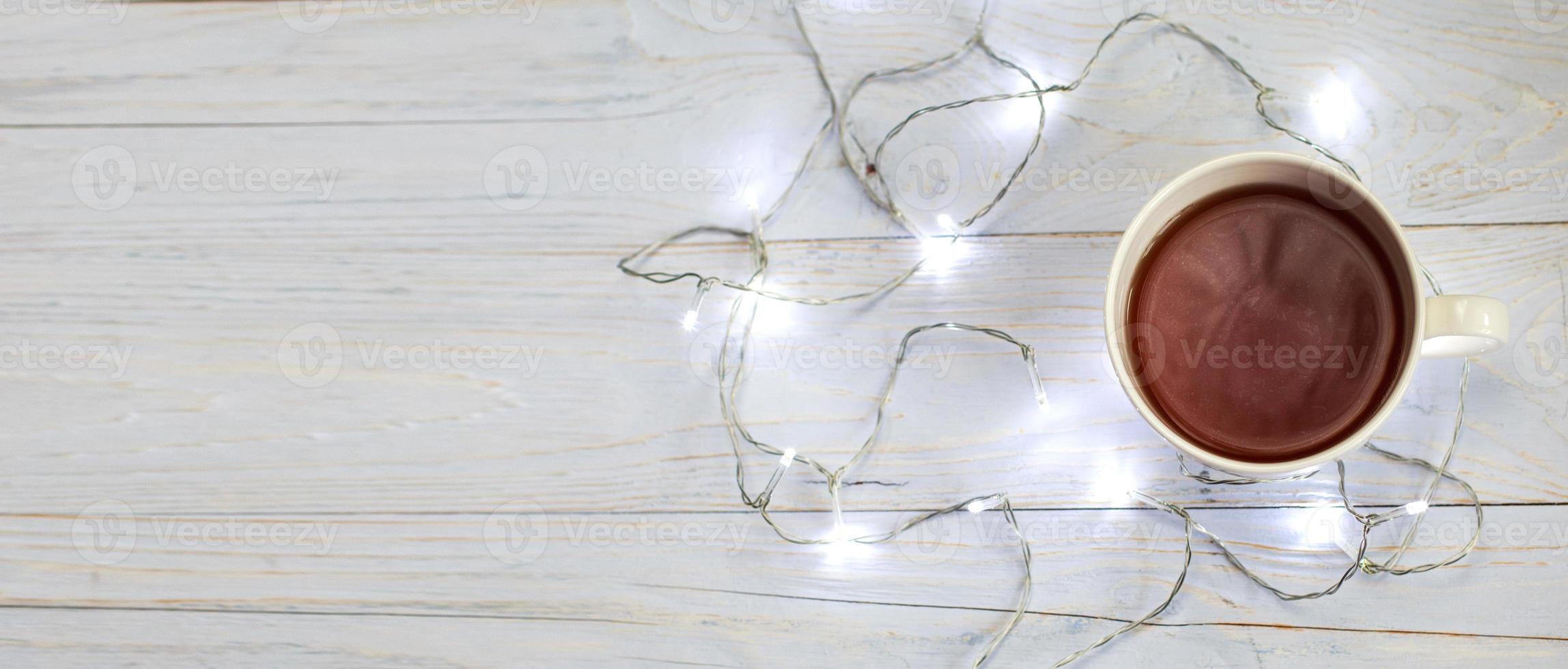 Cup of tea or coffee and garland on light wooden background. banner photo