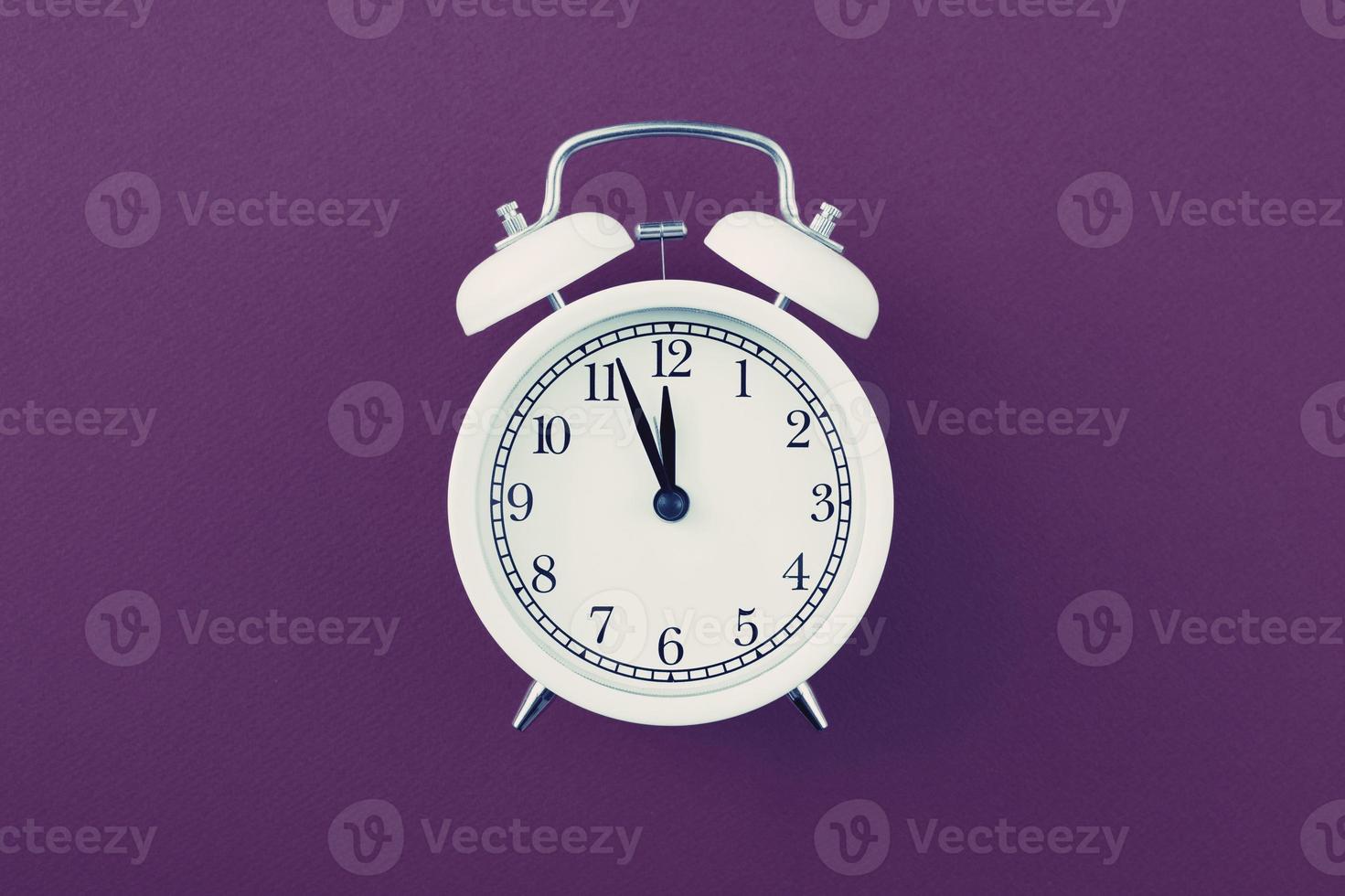 Alarm clock showing five minutes to twelve on a purple background. photo