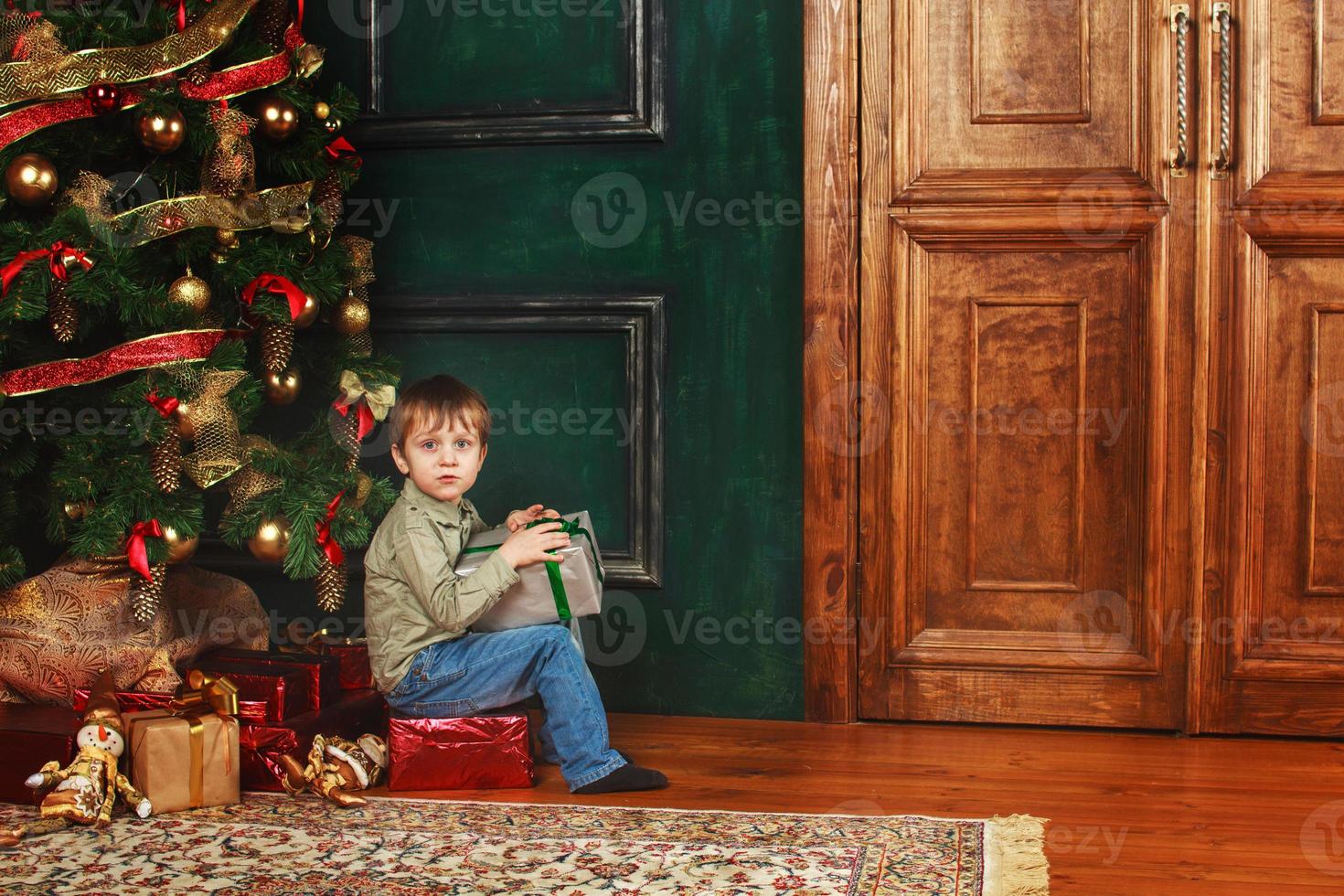 child boy sitting under the Christmas tree with gift box photo