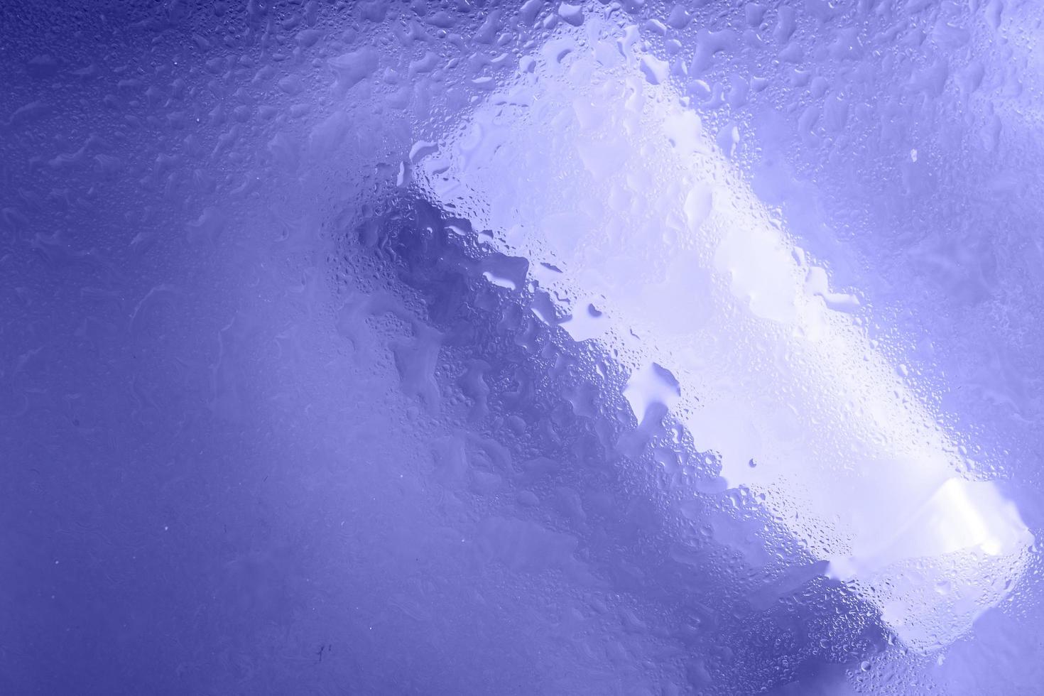 crema facial y de manos bajo una superficie de vidrio con agua sobre fondo morado. foto