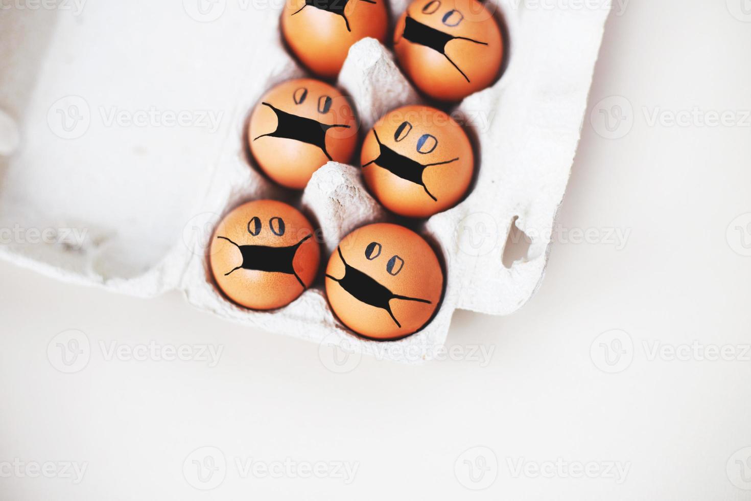 chicken eggs with drawn medical mask on egg carton on white background. Easter eggs holidays decoration. photo