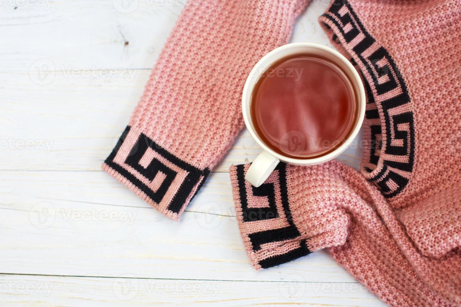 Cup of hot coffee with knitted sweater on wooden table, winter morning concept photo