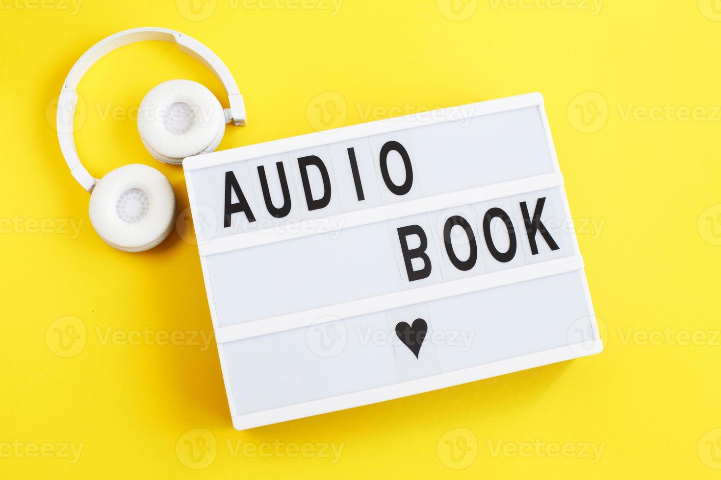 inscription audiobook on a light box with modern white headphones on a yellow background photo