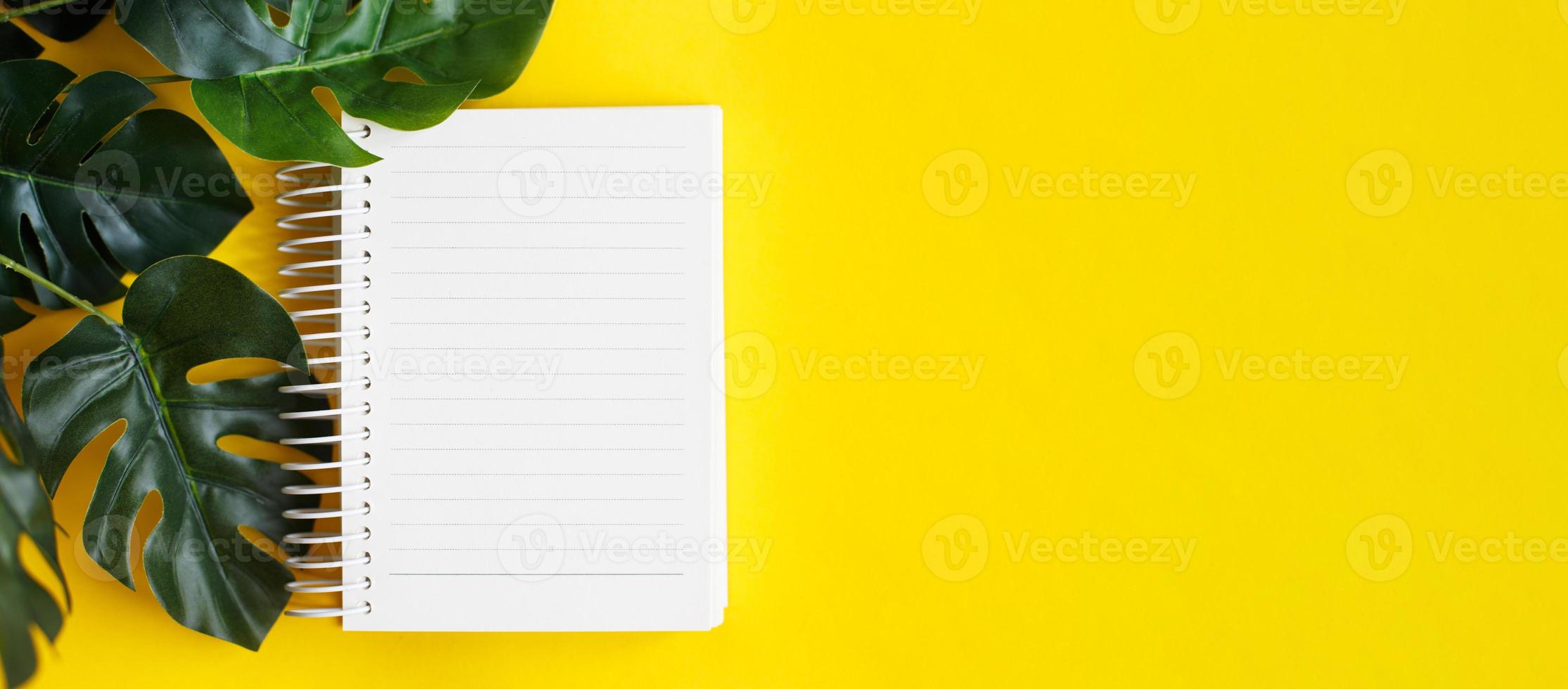 Top view of blank note paper and monstera leaf on yellow background photo