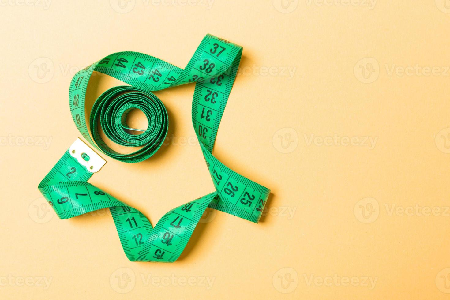 Top view of measure tape curtailed into a spiral with copy space. Concept of sewing accessory or healthy diet on orange background photo