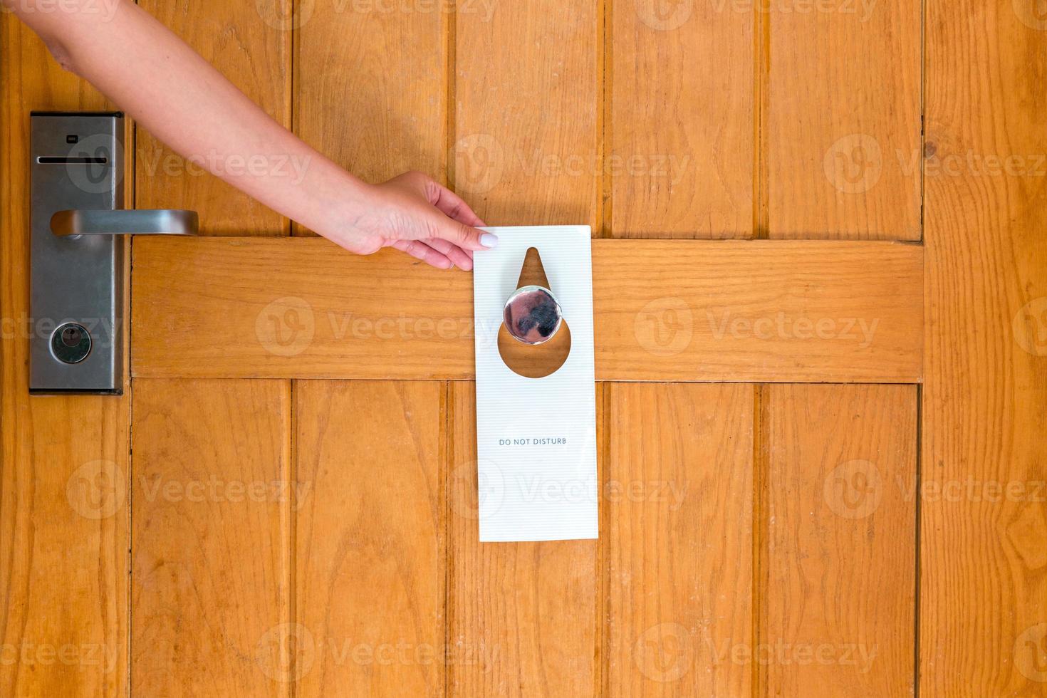 Woman hand holding and hangs signboard do not disturb on the door in hotel photo