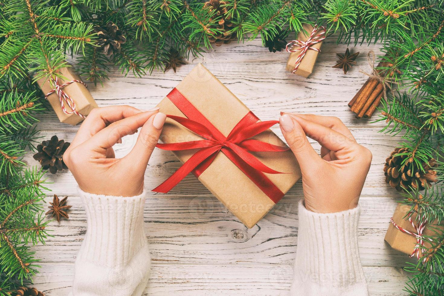 manos femeninas sosteniendo una caja de regalo hecha a mano en papel reciclado sobre fondo de mesa de madera blanca. concepto de preparación navideña, fondo de envoltura de regalos. tonificado foto