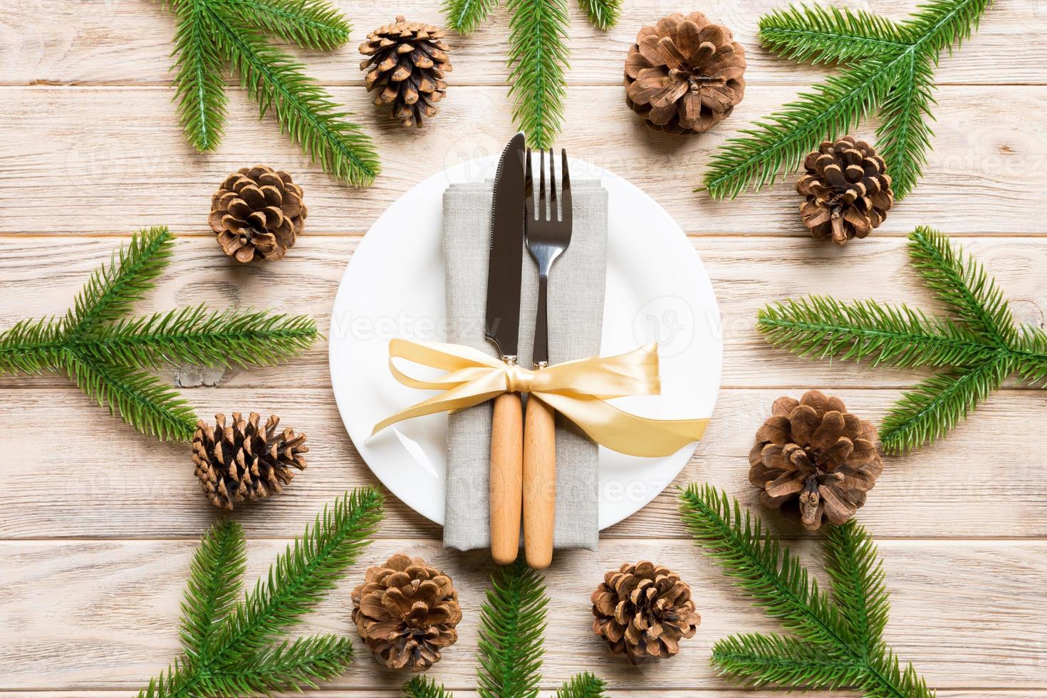 New Year set of plate and utensil on wooden background. Top view of holiday dinner decorated with pine cones. Christmas time concept photo