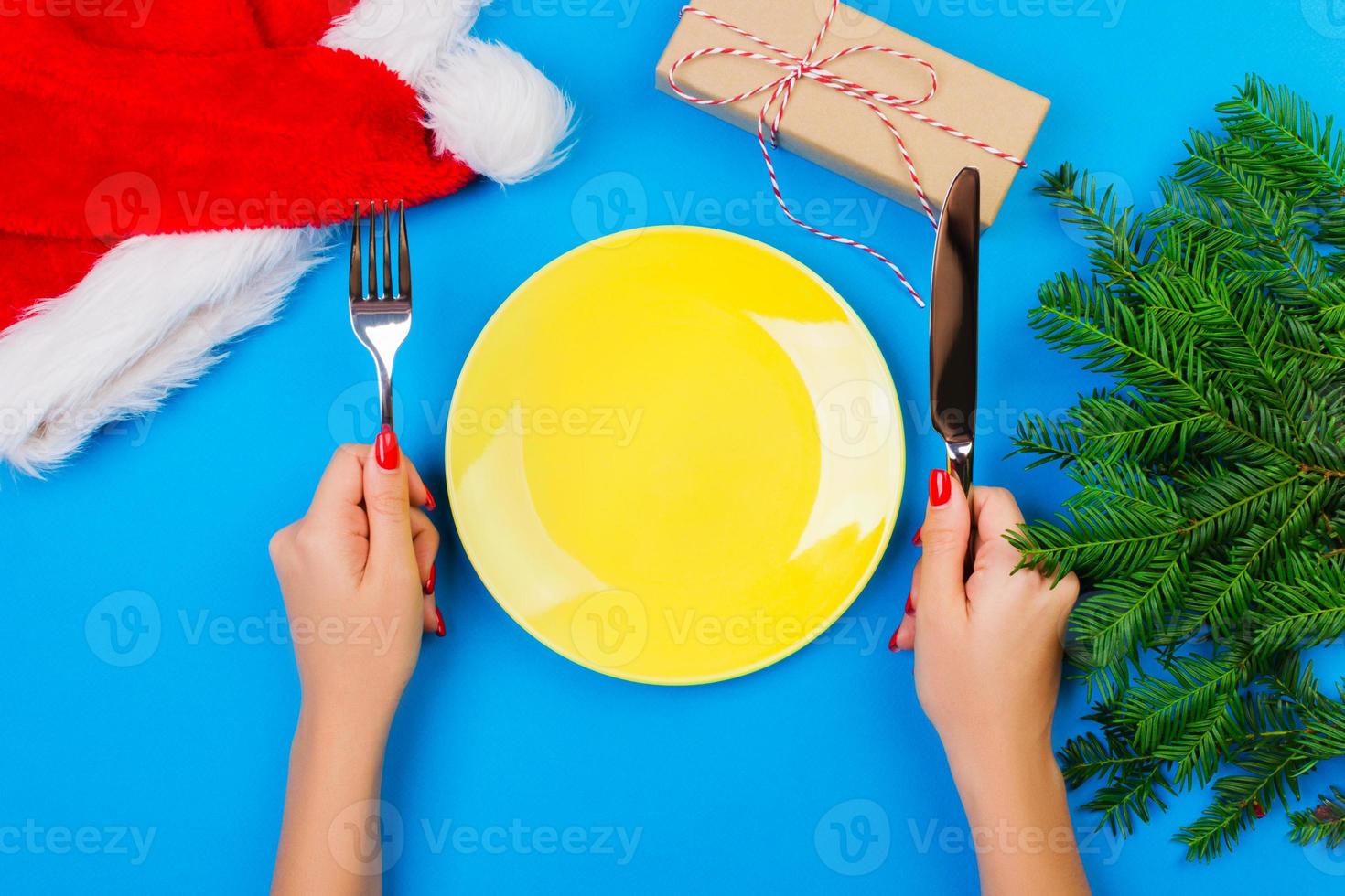 Hungry woman waiting for meal. empty yellow plate on a blue background with Christmas branches, santa hat and gift box. perspective view for your design photo