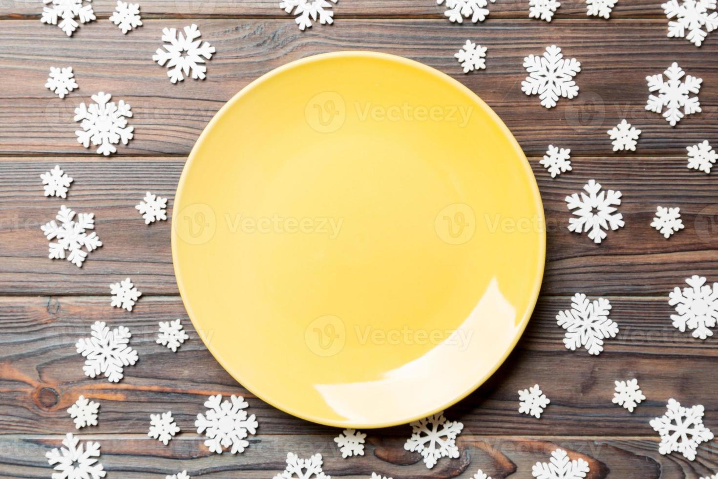 Top view of empty plate surrounded with snowflakes on wooden background. New Year dinner concept photo