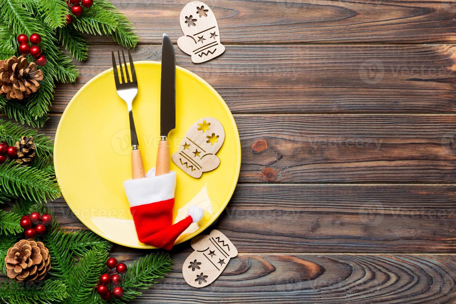Top view of Christmas dinner on wooden background. Plate, utensil, fir tree and holiday decorations with copy space. New Year time concept photo