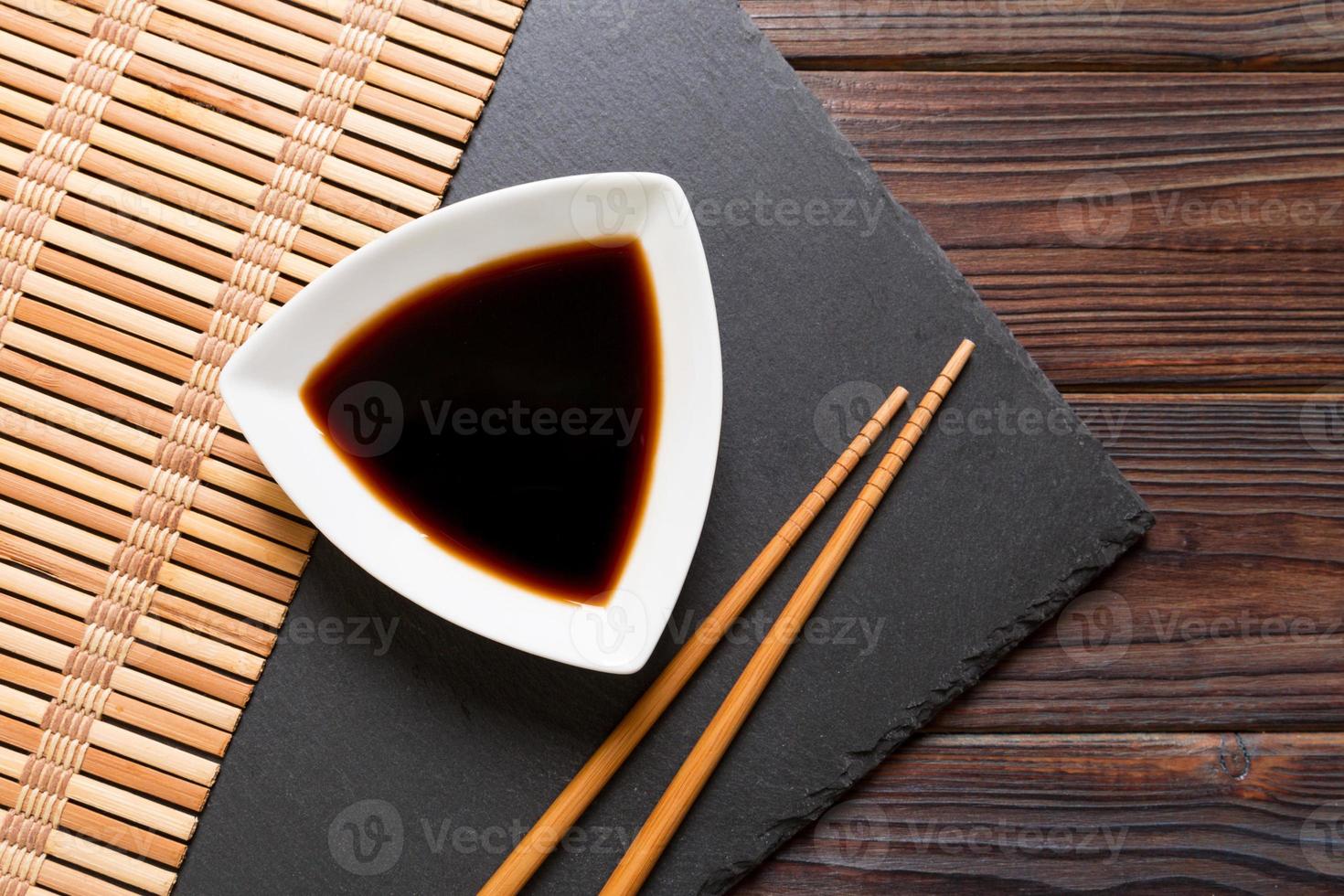 Chopsticks and soy sauce on black stone plate, wooden background with copy space photo