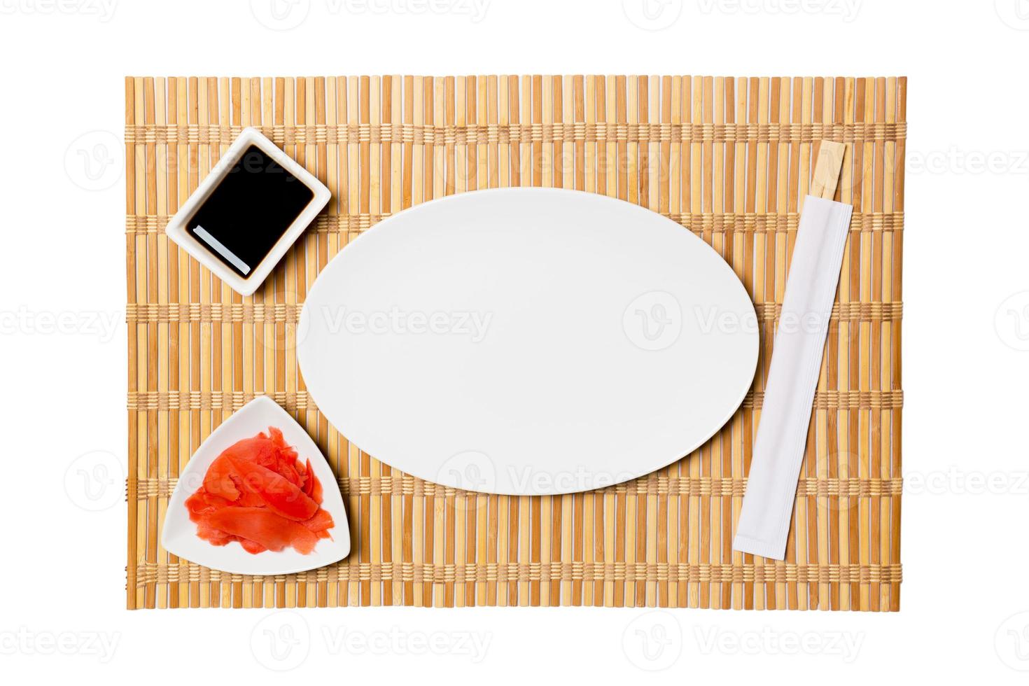 Empty oval white plate with chopsticks for sushi and soy sauce, ginger on yellow bamboo mat background. Top view with copy space for you design photo