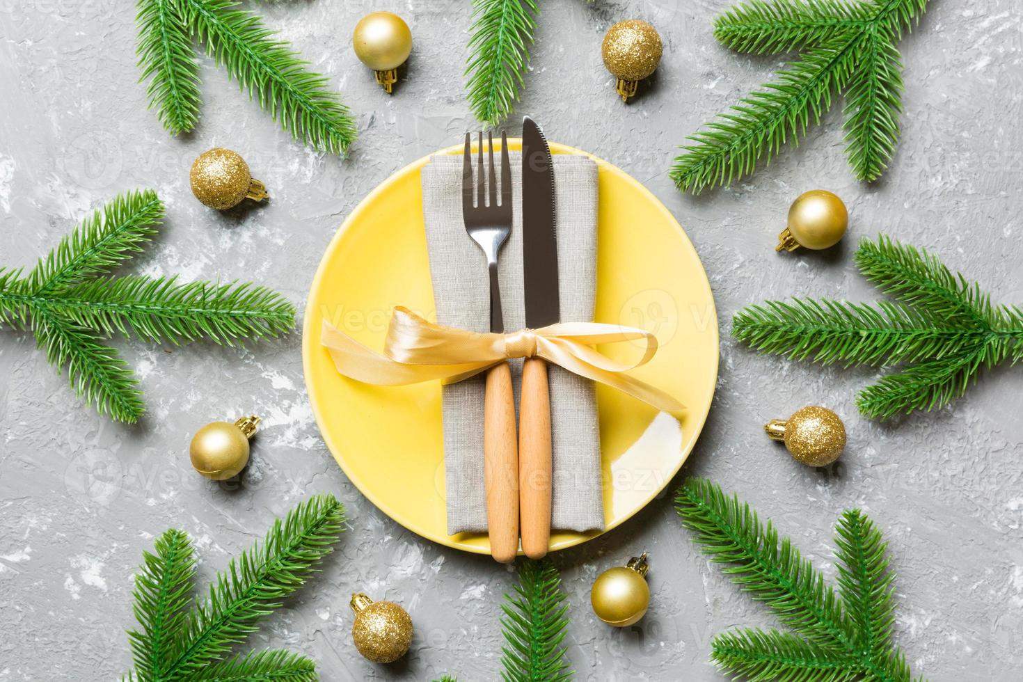 Top view of New Year dinner on festive cement background. Composition of plate, fork, knife, fir tree and decorations. Merry Christmas concept photo