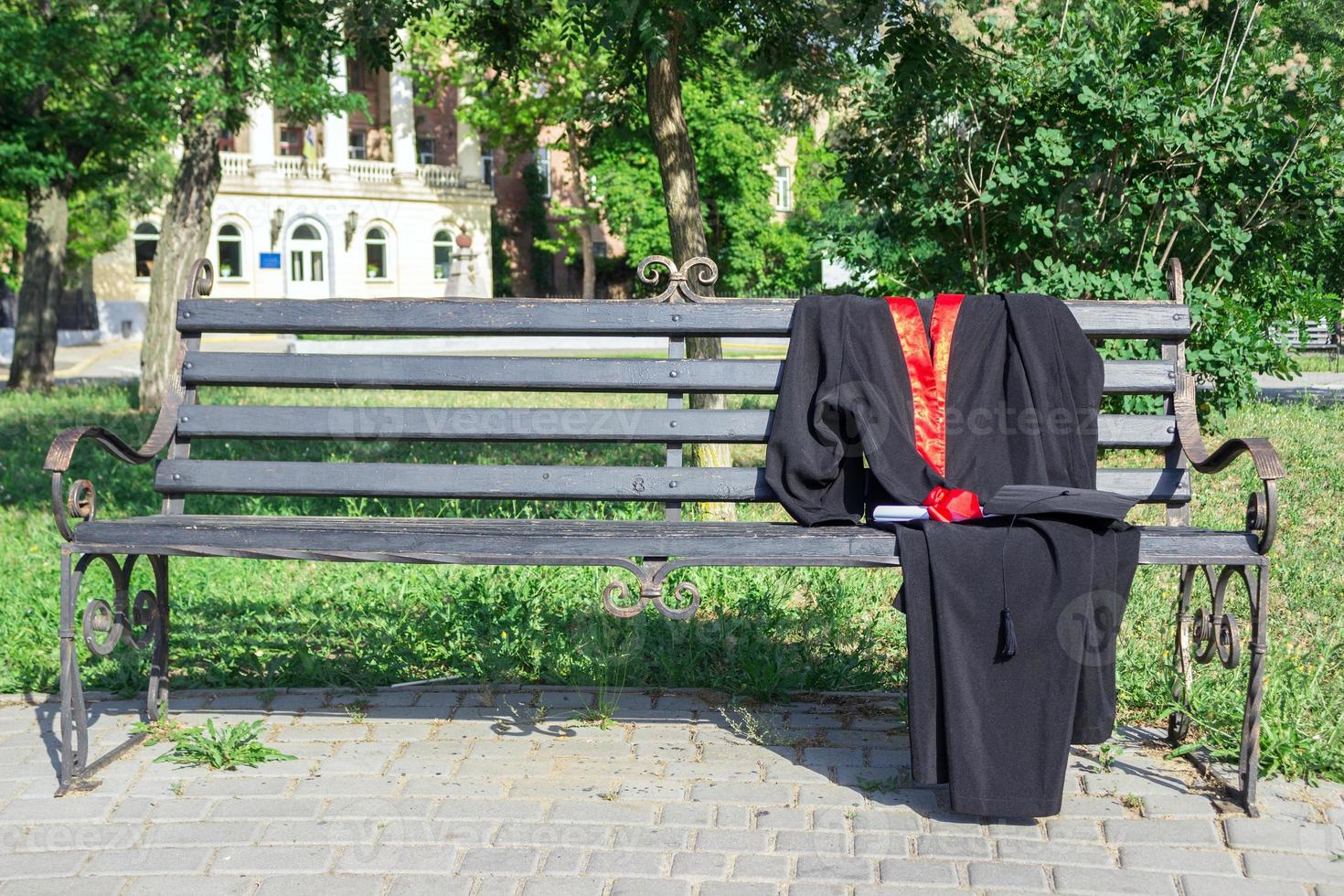 gorra de graduación, sombrero con borla negra, manto con un grado de papel en un banco del parque foto