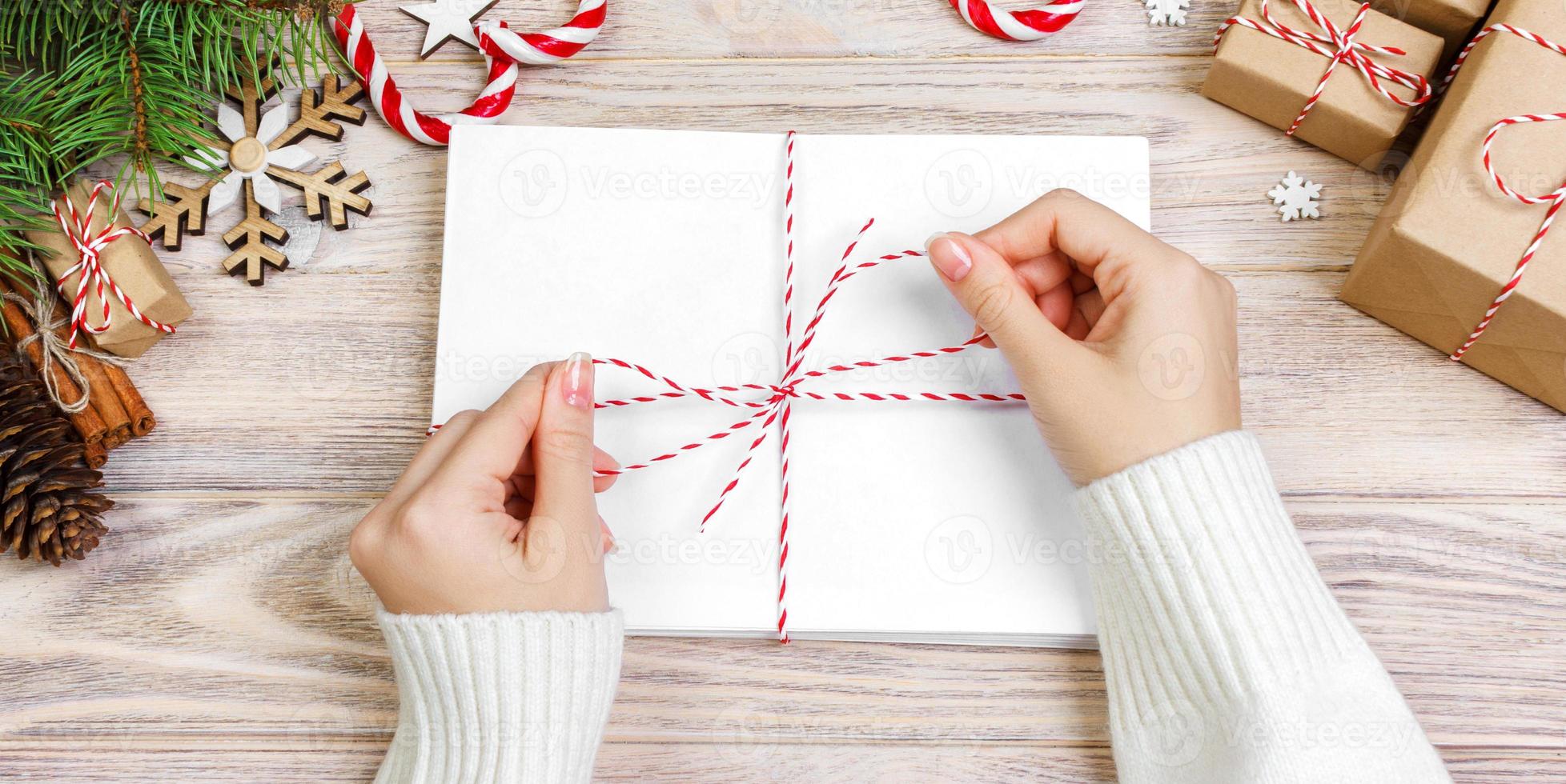 Many envelopes tied with rope. Close-up top view of famale hands with envelope. Pine cones and christmas decoration on old wooden table, desk photo