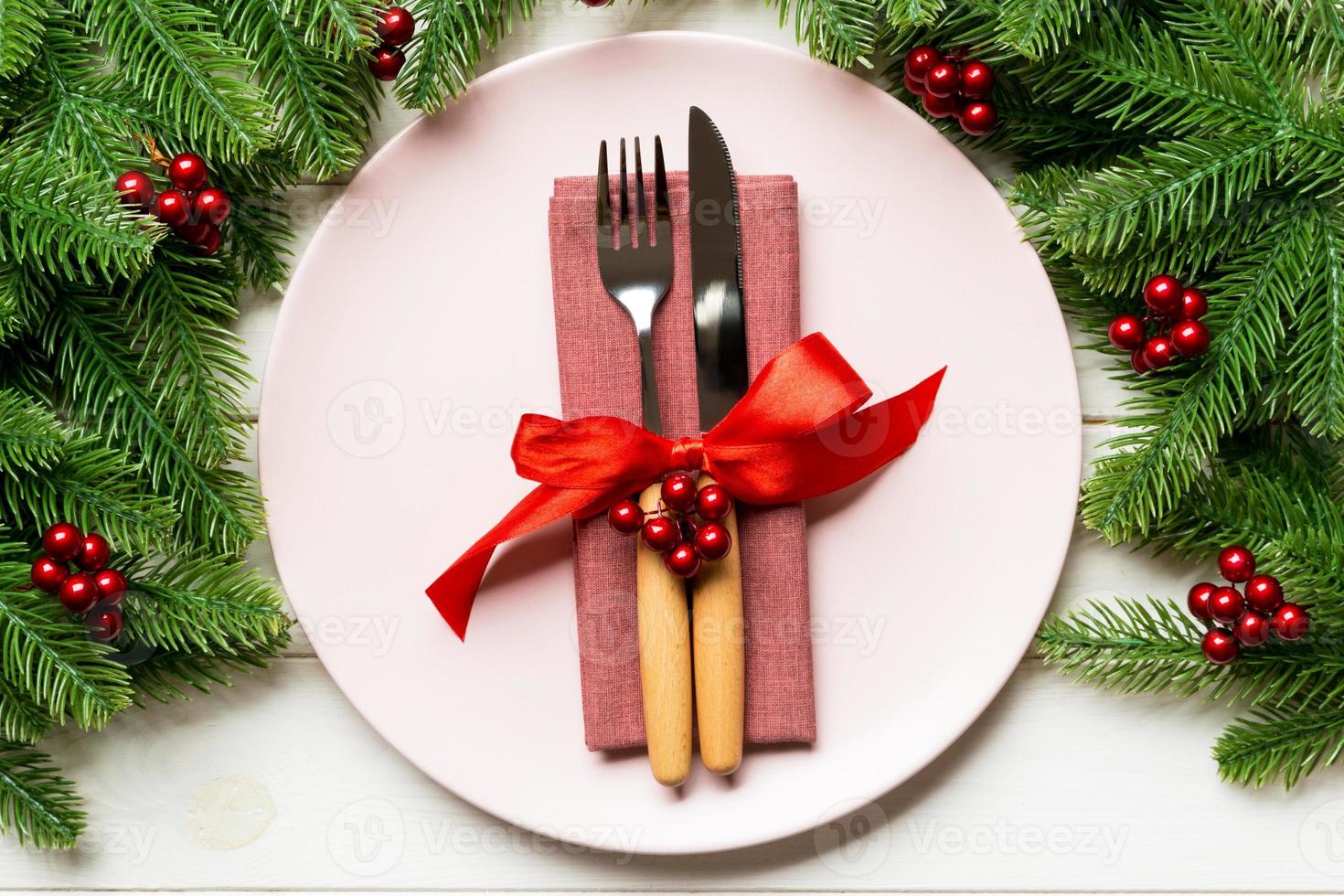Holiday composition of plate and flatware decorated with fir tree on wooden background. Top view of Christmas decorations. Festive time concept photo