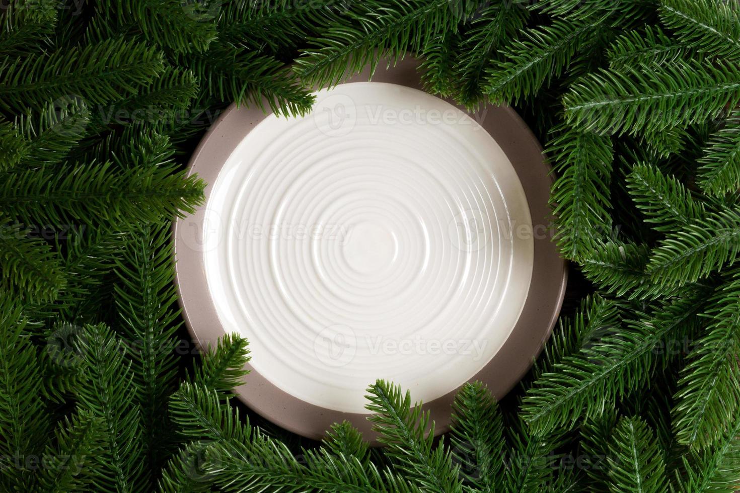 Top view of white plate surrounded with fir tree branches. Christmas dinner concept with copy space photo