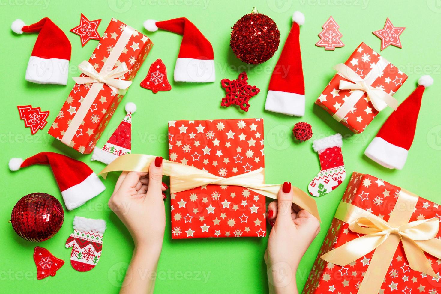 Top view of female hands holding a Christmas present on festive green background. Santa hats and holiday decorations. New Year holiday concept photo