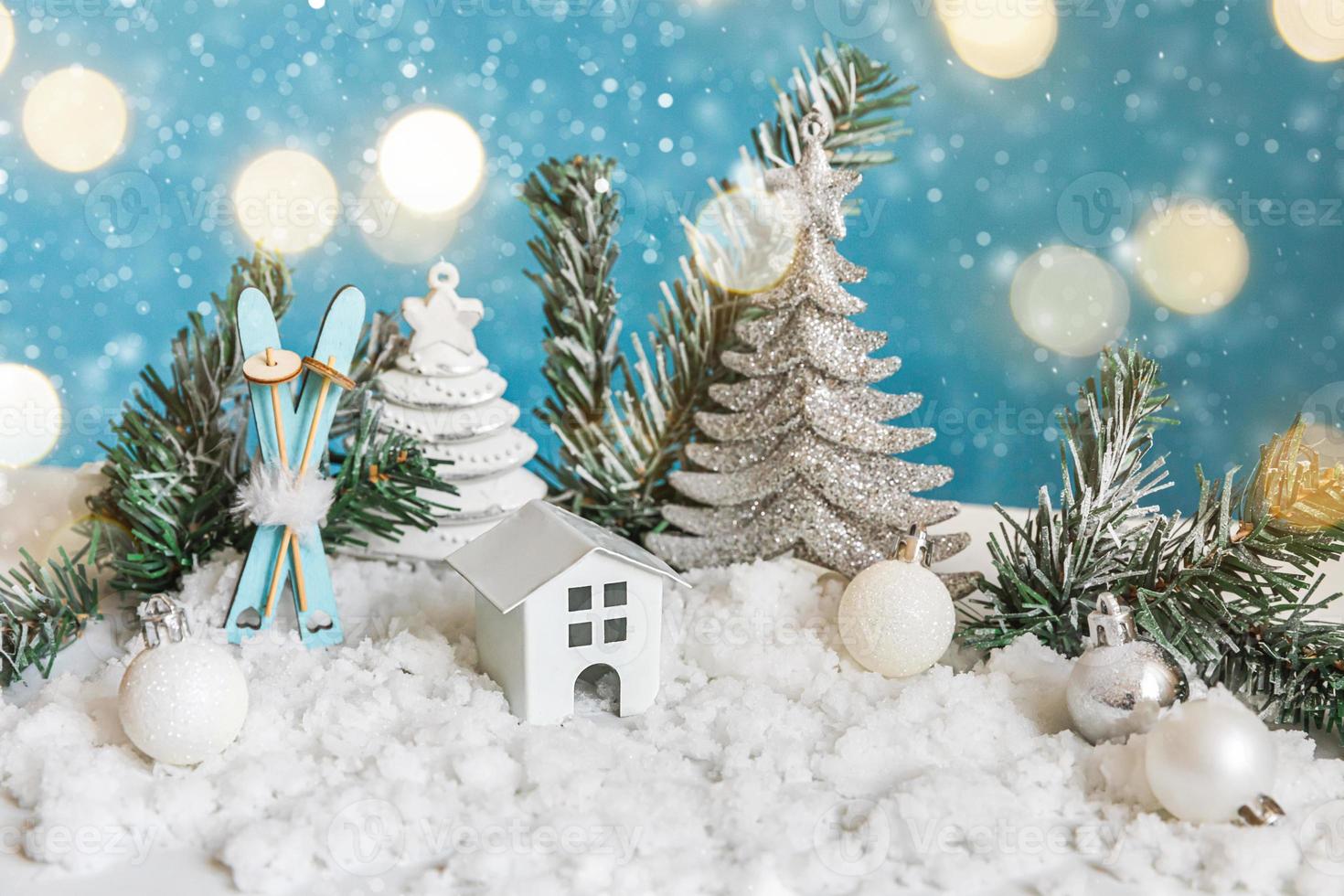 Abstract Advent Christmas Background. Toy model house and winter decorations ornaments on blue background with snow and defocused garland lights. Christmas with family at home concept. photo
